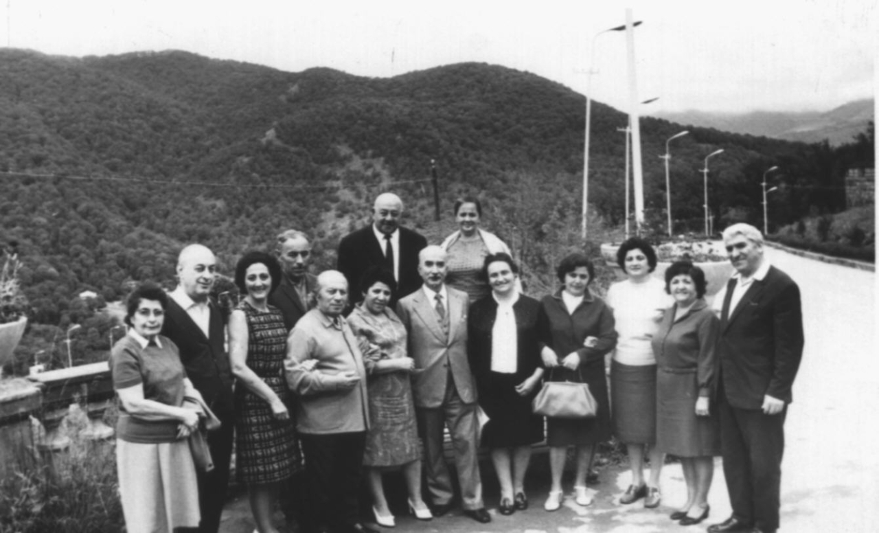 Ե. Քոչարը /ձախից չորրորդը/ մի խումբ մարդկանց հետ անտառապատ լեռների ֆոնին.  ձախից առաջինը՝ գեներալ Մարտիրոսյանի կինը, երկրորդը՝ գեներալ Մարտիրոսյանը,  երրորդը՝ Գավուկի կինը,  ութերորդը՝ Մ. Մկրտչյանը, կողքինը՝  Մարուսյան,  [1970–ականներ]