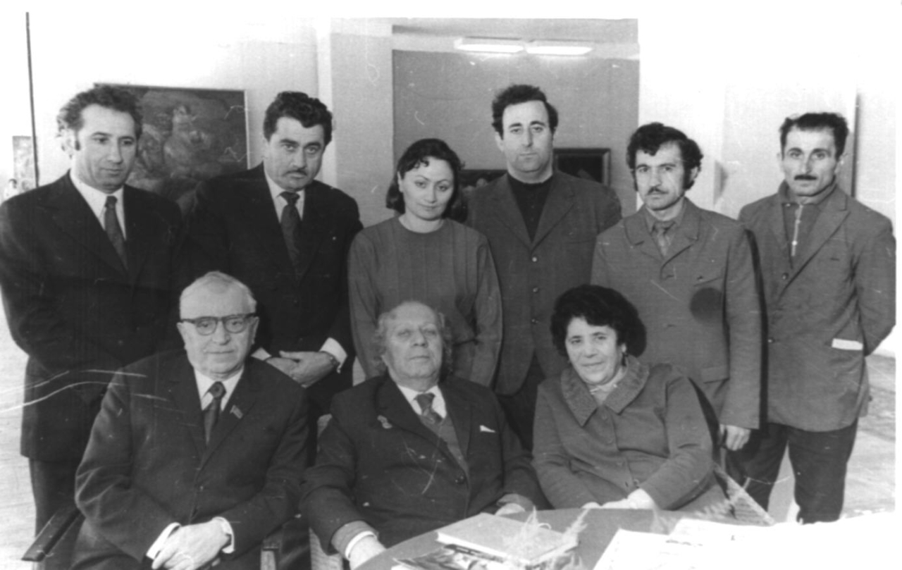 Մի խումբ մարդիկ Երվանդ Քոչարի անհատական ցուցահանդեսի բացման օրը. առաջին շարքում ձախից աջ՝ Ս.Գրիգորյանը, Ե.Քոչարը, Մ. Մկրտչյանը, երկրորդ շարքում ձախից երկրորդը՝ Վլ.Աբրահամյանը, չորրորդը՝ Լ.Ադիյանը, Բաքու, 4 ապրիլի, 1974 